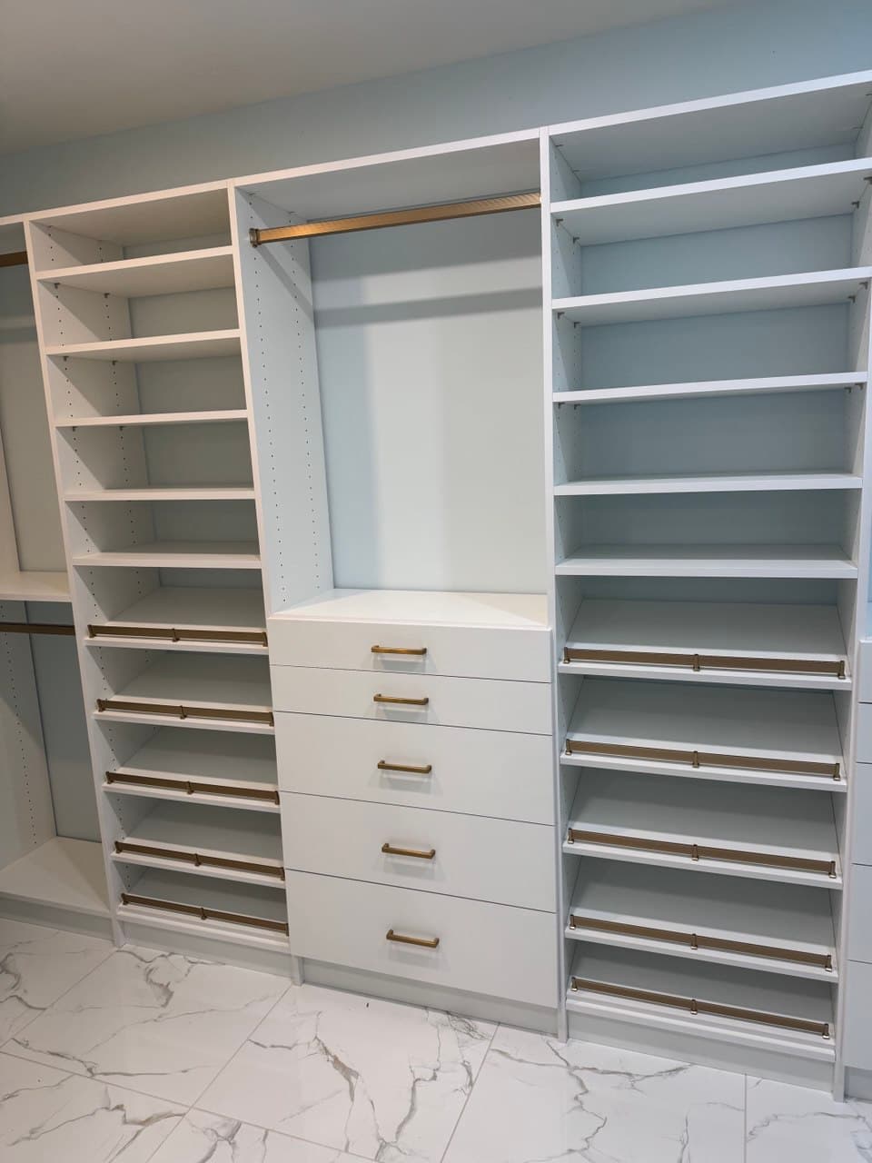White custom closet with brass hardware and marble flooring