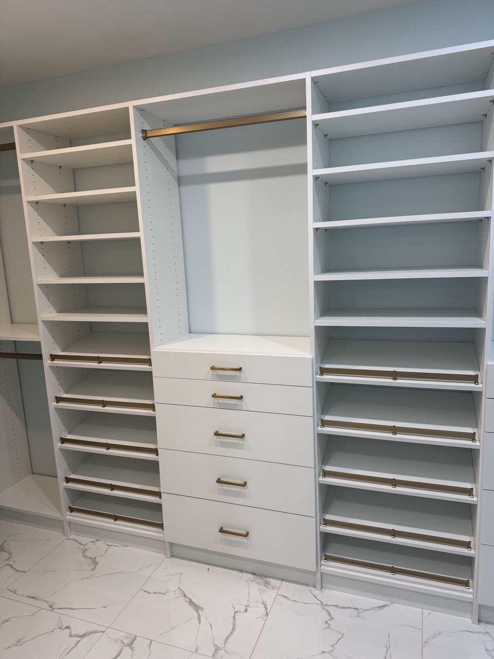 White custom closet with brass hardware and marble flooring